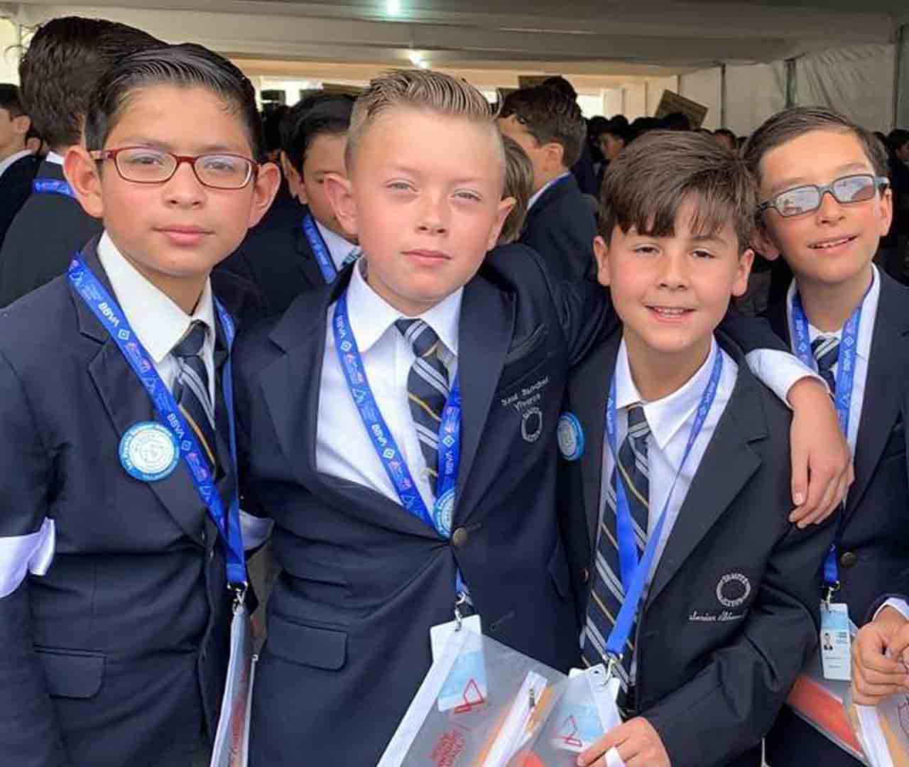 Cuatro alumnos de primaria vistiendo traje en evento de colegio interamericano.