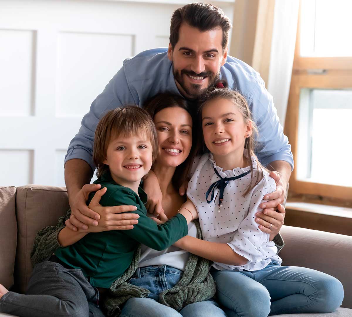 Familia conformada por padre, madre, hija mayor e hijo menor abrazándose.